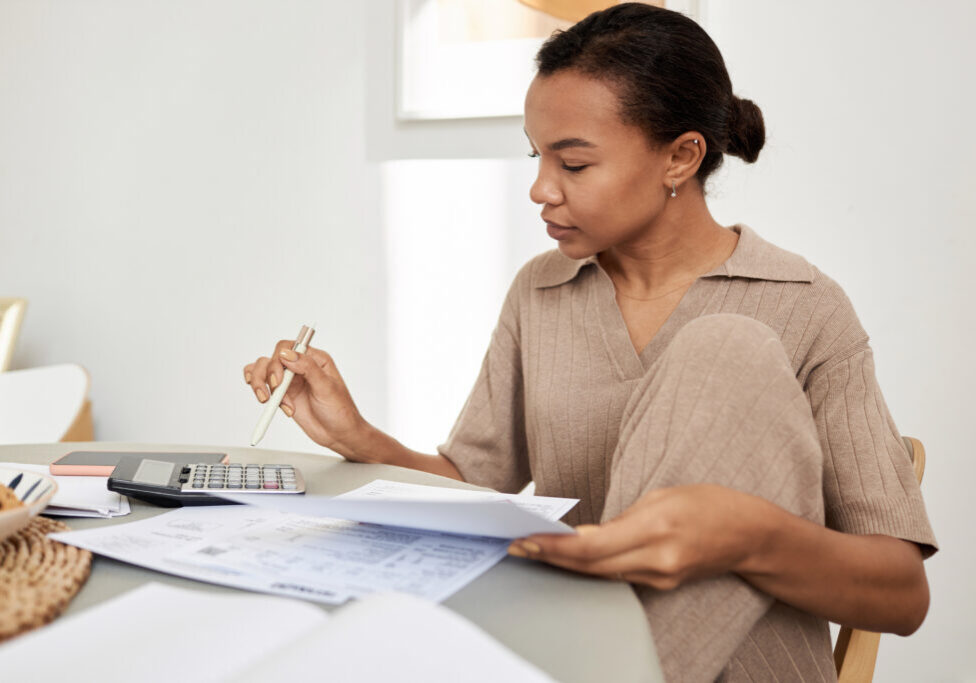 Minimal side view portrait of young Black woman doing taxes at home and using calculator, copy space